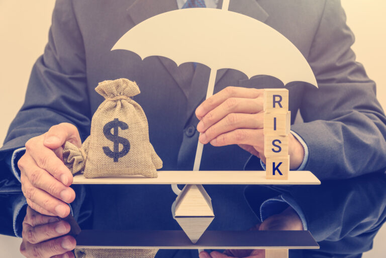 23 03 09 a person with the word risk and a bag of money balanced in front of them on a simple balance with an umbrella over the whole mf dload gettyimages 1058471606