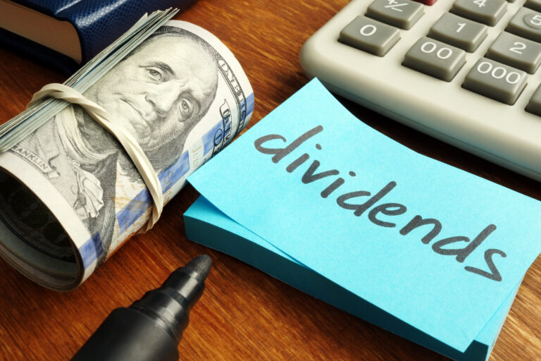 a note saying dividends beside a stack of dollars and a calculator