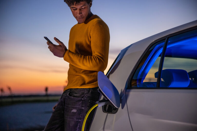 man using mobile phone while charging electric car