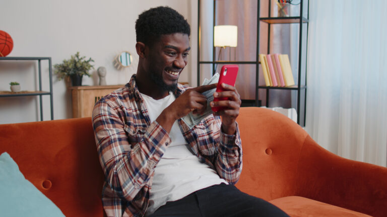 person on a couch smiling while using a smartphone