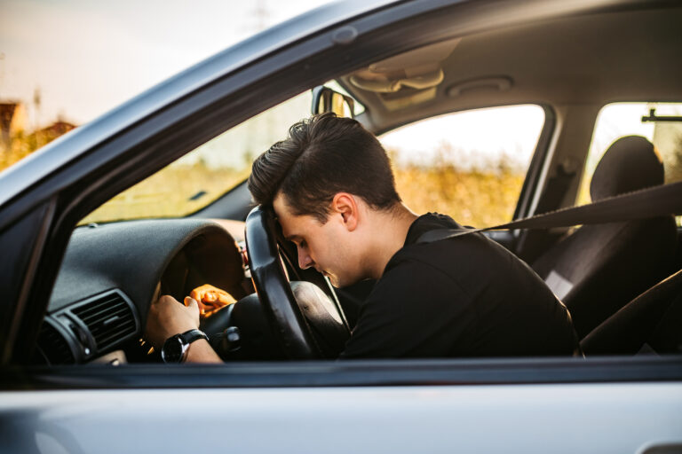 person with head on car steering wheel