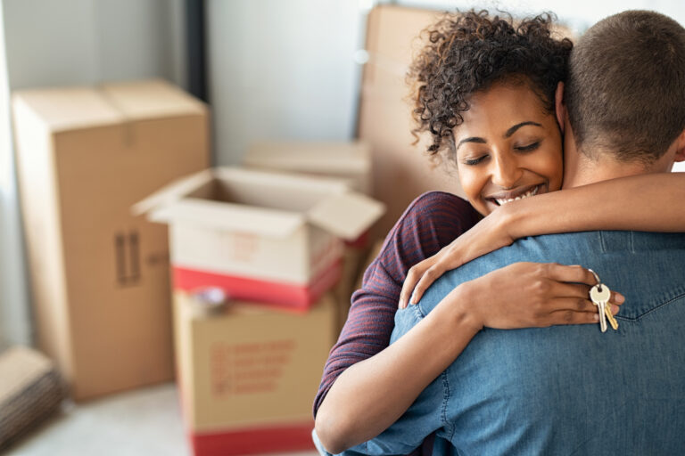 two people hugging one holding new house keys in front of moving boxes