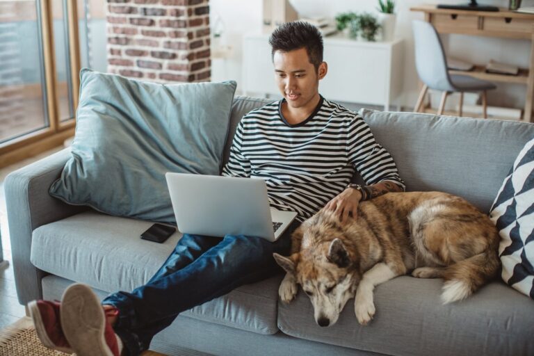 young man on laptop on couch with dog QRysiD0