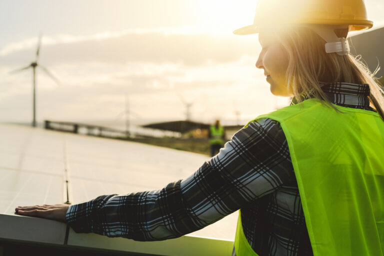 a person installing a solar panel near a wind farm