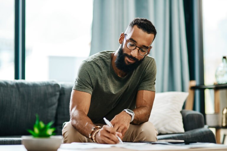 adult writing with pen on table and sofa