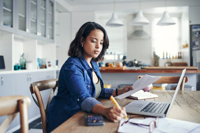 person holding document and writing note with laptop in front of them