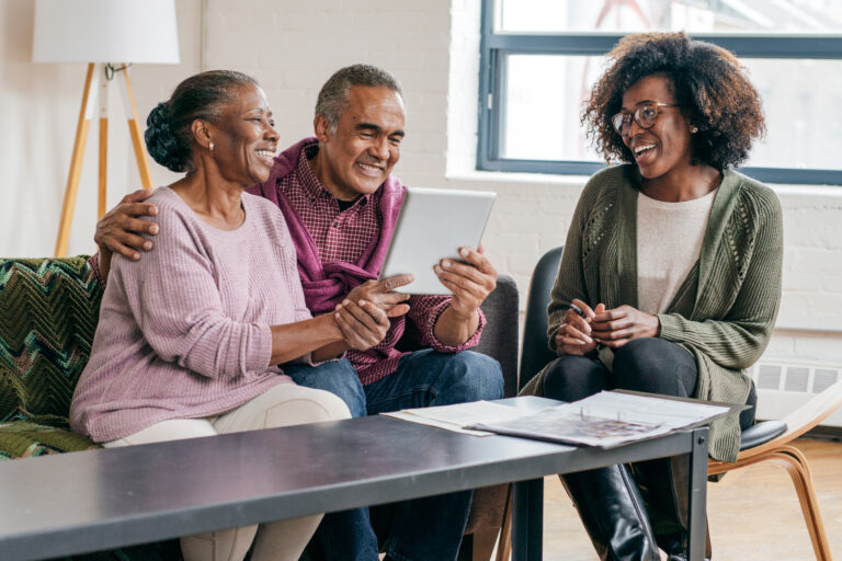 three people sitting at a table looking at documents and a tablet