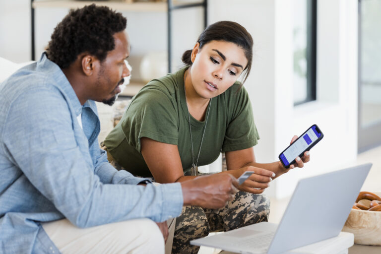 two people look at a laptop and phone while on person holds credit card