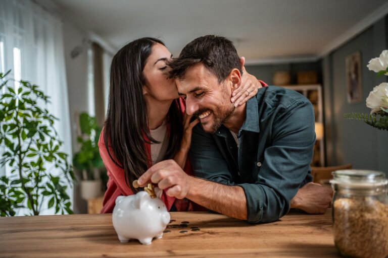 an excited couple putting money in a piggy bank