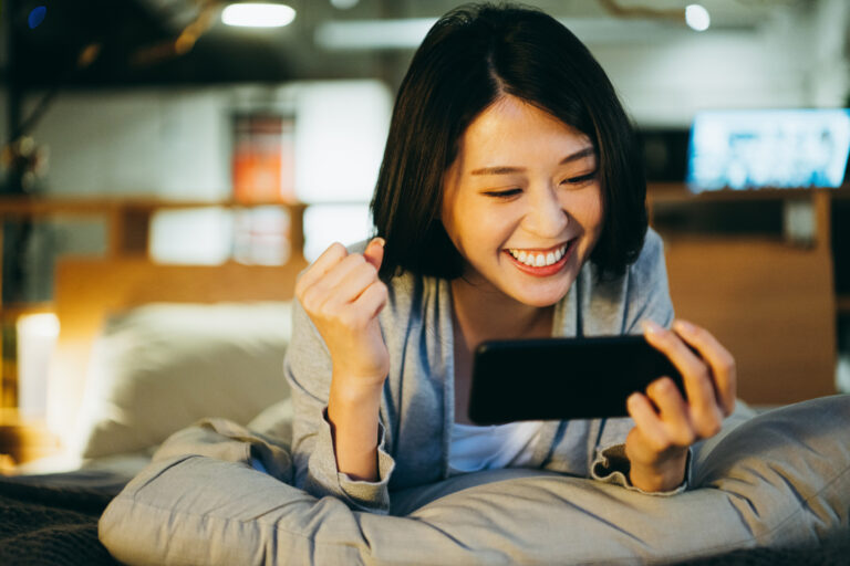 excited person lying on bed looking at phone screen