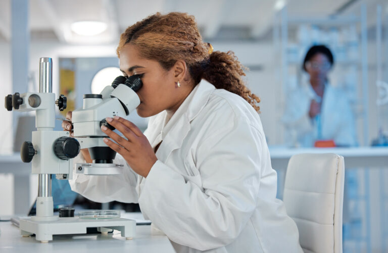 scientist looks into microscope while sitting at bench in laboratory