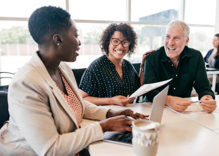 three people sitting at a table smiling and looking at paperwork