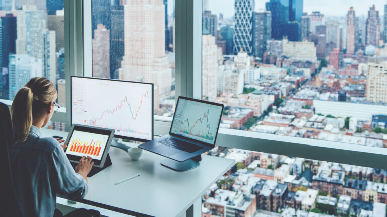 person at big city office window with multiple screens