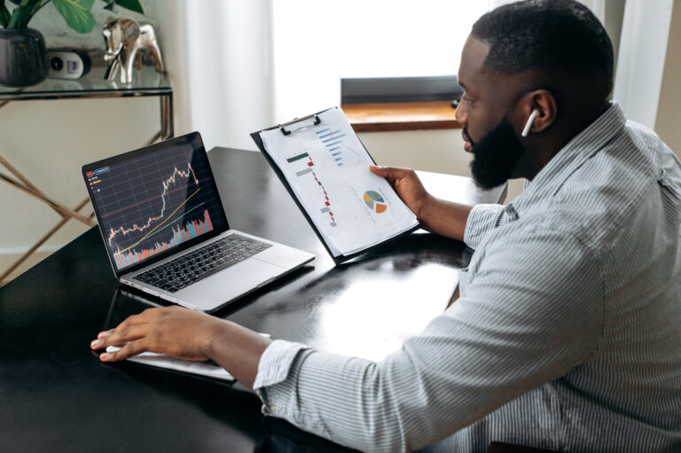 a person holding a clipboard while looking at stock charts on a laptop