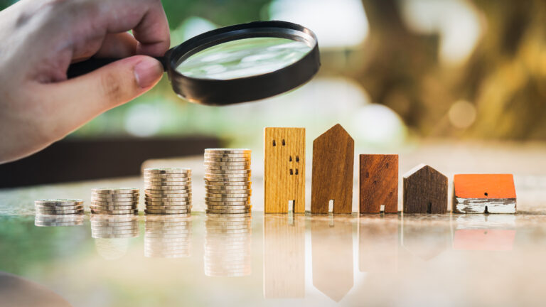 a person holding a magnifying glass looking at a row of rising coins and buildings