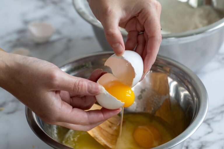 hands cracking egg into metal bowl