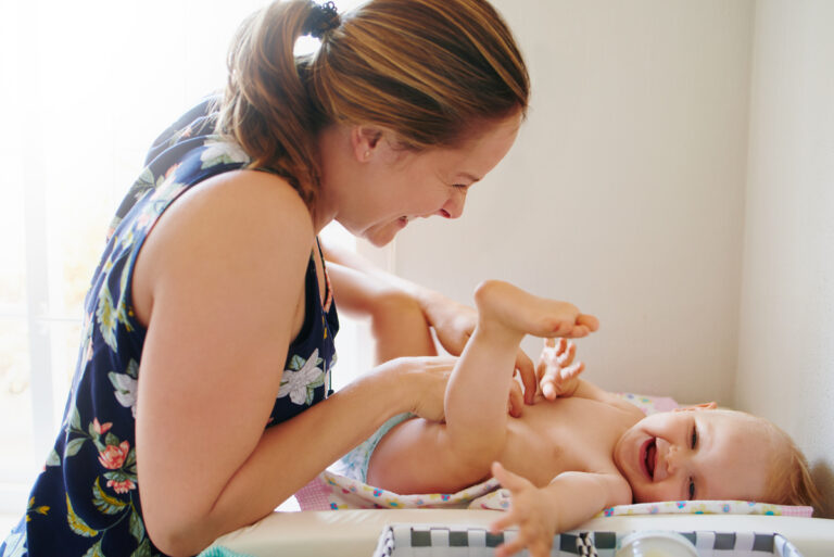a baby smiles while an adult changes its diaper
