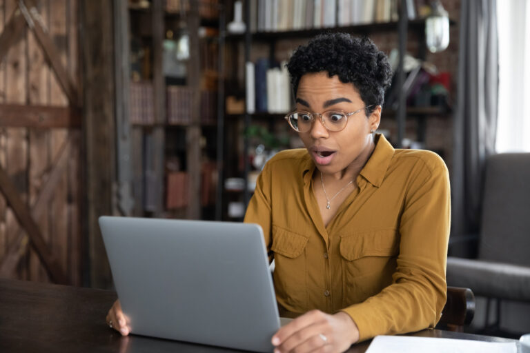 a person sitting at a table looks at a laptop computer screen in a surprised manner